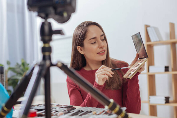 Молодая внимательная женщина сидит за столом с теневой палитрой
