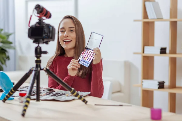 Blogueiro de moda positiva sorrindo e mostrando paletas de sombra — Fotografia de Stock