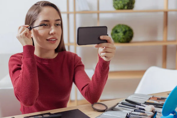 Blogueuse beauté calme portant le mascara et regardant son smartphone — Photo