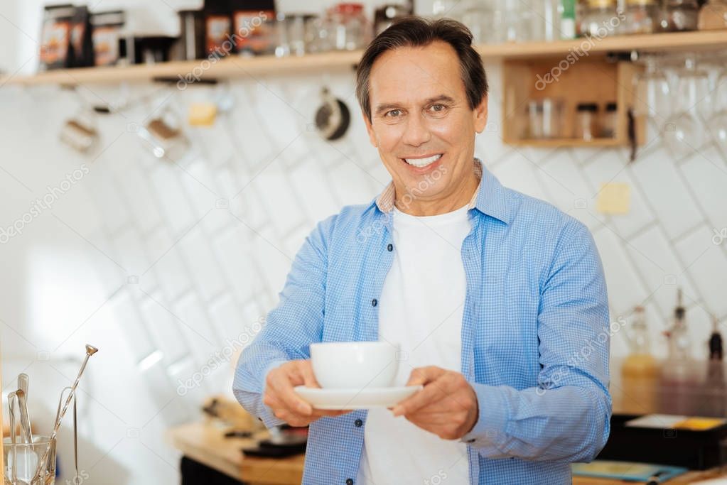 Handsome pleasant man smiling and giving a cup.