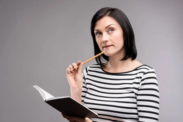 Pleasant young woman thinking before making notes — Stock Photo, Image
