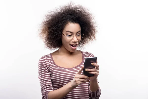Curly-haired woman being surprised while reading news on phone — Stock Photo, Image