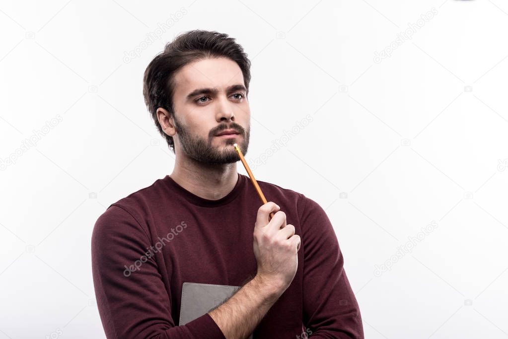 Handsome man pressing tip of pencil to chin and thinking