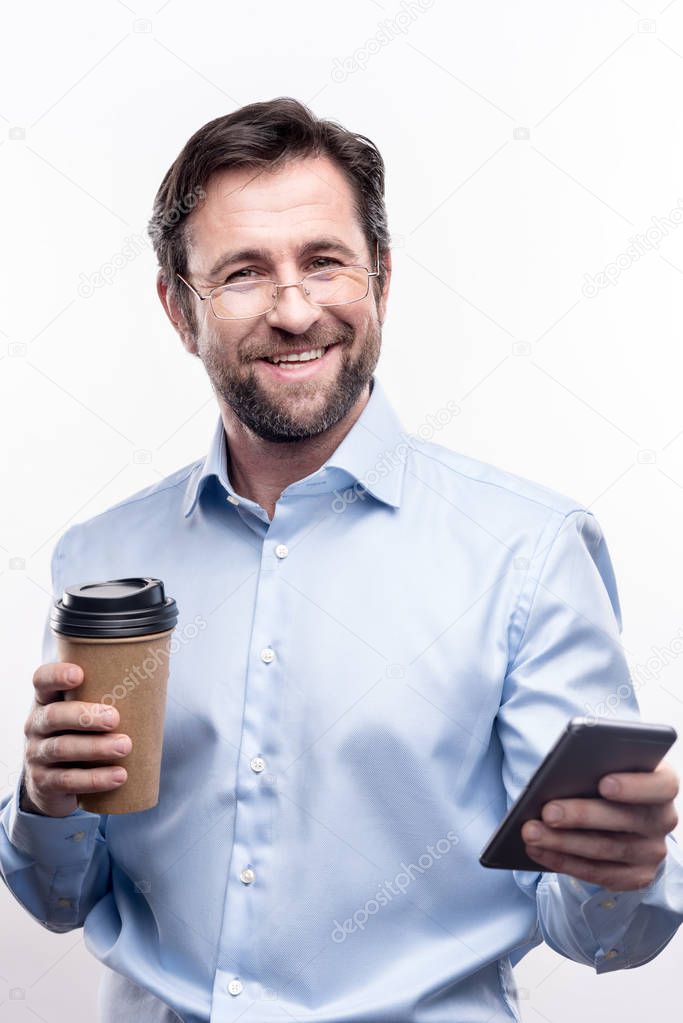 Charming businessman posing with coffee cup and phone in hands