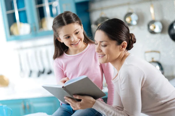 Glad tjej och hennes mamma som tittar genom en bok — Stockfoto