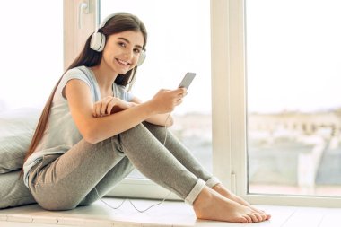 Genç kız pencere pervazına müzik dinlerken poz