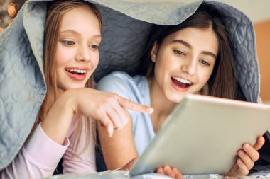 Battaniyenin altında video izlerken neşeli kızlar