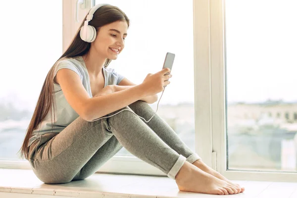 Bastante adolescente escuchando música en alféizar de la ventana —  Fotos de Stock