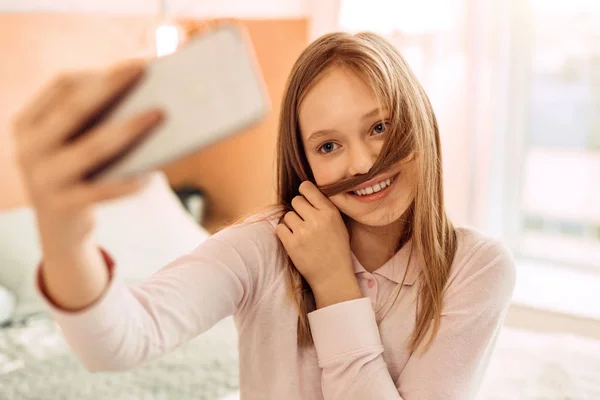 Menina colocando fio de cabelo sob o nariz enquanto toma selfie — Fotografia de Stock