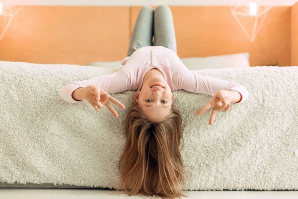 Pleasant teenage girl hanging her head from bed and posing — Stock Photo, Image