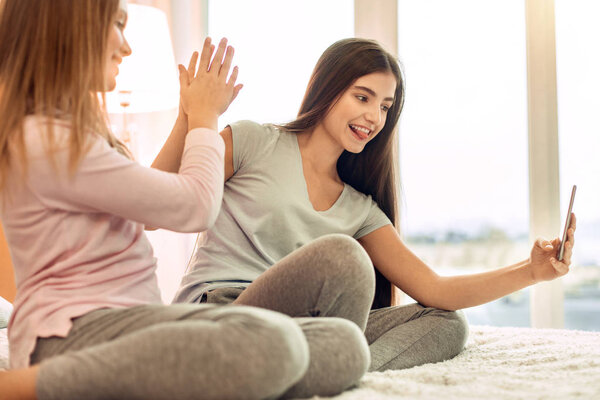 Upbeat sisters high-fiving each other and taking selfie