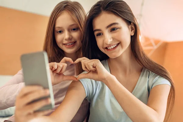 Lindas irmãs fazendo um coração ao tomar selfie — Fotografia de Stock