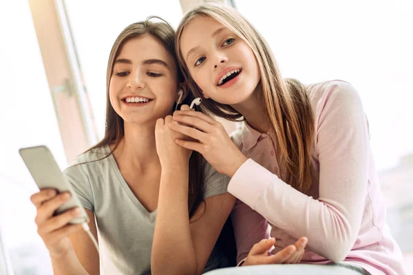 Bonitas irmãs adolescentes compartilhando um par de fones de ouvido — Fotografia de Stock