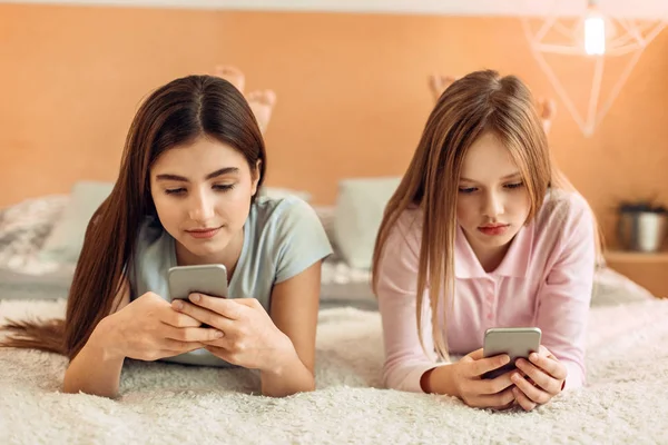 Adolescentes deitadas na cama e usando seus telefones — Fotografia de Stock