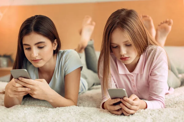 Красивые девушки лежат на кровати и сосредоточены на своих телефонах — стоковое фото