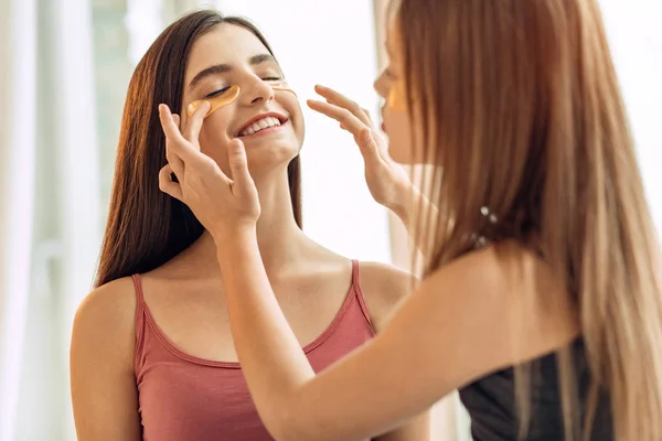 Caring girl adjusting under-eye patches on sisters face — Stock Photo, Image