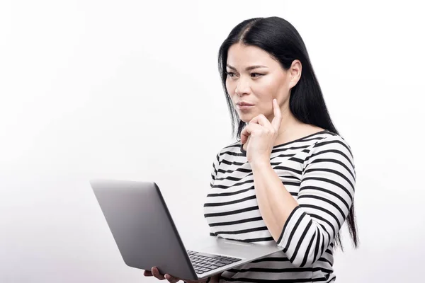 Affascinante donna dai capelli scuri pensando mentre si lavora sul computer portatile — Foto Stock