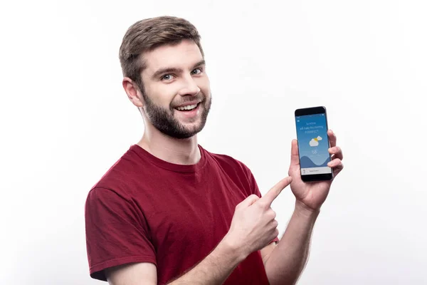 Sorrindo jovem mostrando aplicação do tempo no telefone — Fotografia de Stock