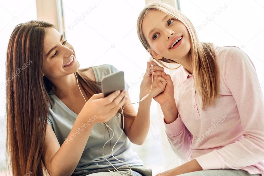Pleasant girl giving earphone with her younger sister