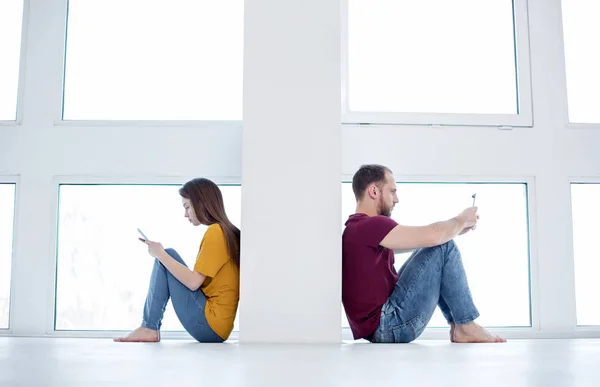 Sad woman and man sitting on the floor typing — Stock Photo, Image