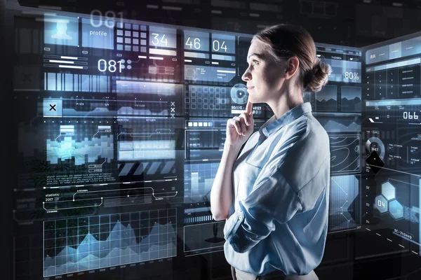 Young woman thoughtfully looking at the screen and touching her chin — Stock Photo, Image