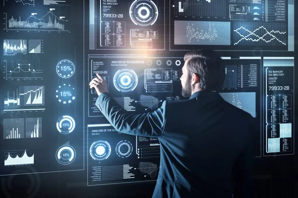 Elegant programmer standing in front of a futuristic device and touching it — Stock Photo, Image