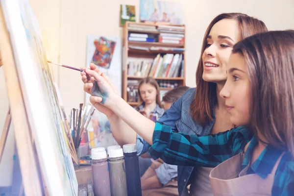 Jovem mulher ajudando estudante com pintura — Fotografia de Stock