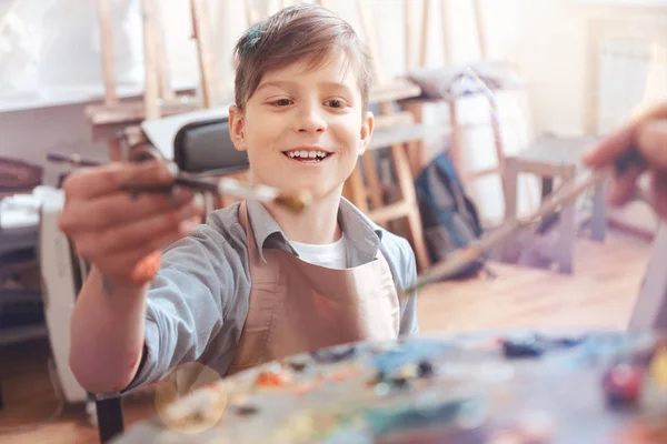 Emocionado adolescente sonriendo ampliamente mientras mezcla pinturas — Foto de Stock