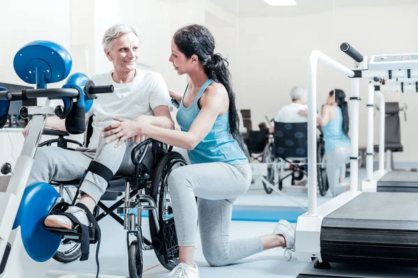 Gelukkig oude man in de rolstoel en zijn lachende trainer — Stockfoto