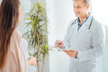 Neşeli doktor hamile kadın ile randevu sırasında notlar almak