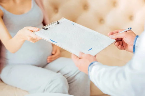 Close up of doctor taking clipboard from pregnant woman — Stock Photo, Image