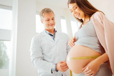 Ayakta ve kadının mide ölçme neşeli yetenekli doktor.