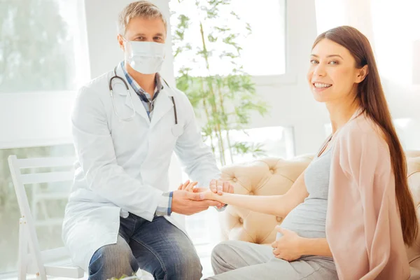 Cheerful doctor checking pulse of expectant mother — Stock Photo, Image