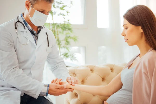 Serious doctor checking pulse of pregnant woman — Stock Photo, Image