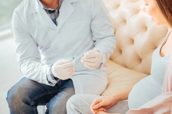 Cuidadoso médico cualificado sentado y sosteniendo la jeringa . —  Fotos de Stock