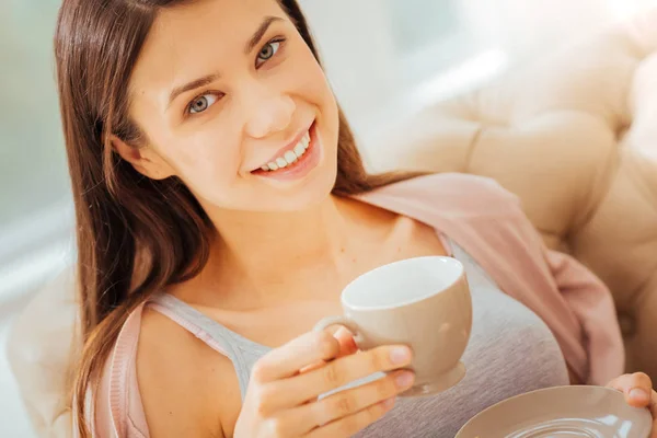 Agradable mujer bonita mirando recto y sosteniendo una taza . — Foto de Stock