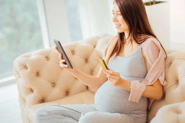 Joyful parturient woman using the tablet and holding credit card. — Stock Photo, Image