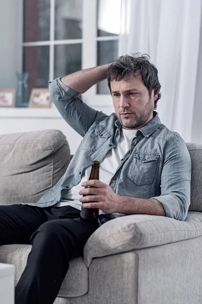 Депресивний чоловік дряпає голову, вживаючи алкоголь сам — стокове фото
