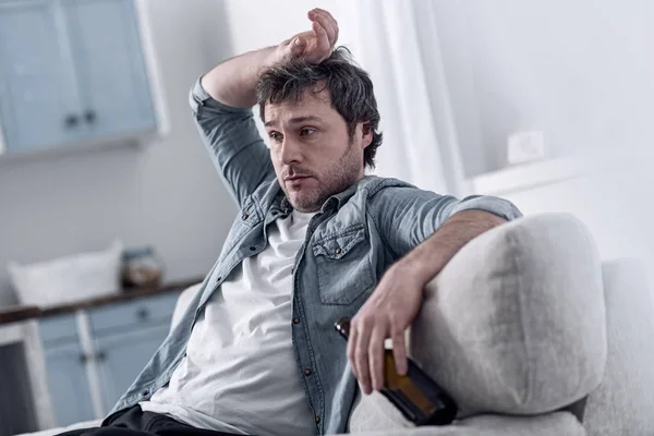 Депрессивный мужчина, сидящий с рукой на руке и пьющий алкоголь — стоковое фото