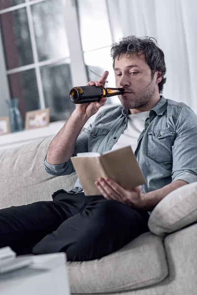Nepořádný člověk, kouření cigaret a pití alkoholu při čtení — Stock fotografie