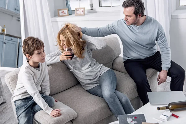 Angry man grabbing hair of his alcoholic wife and looking at her