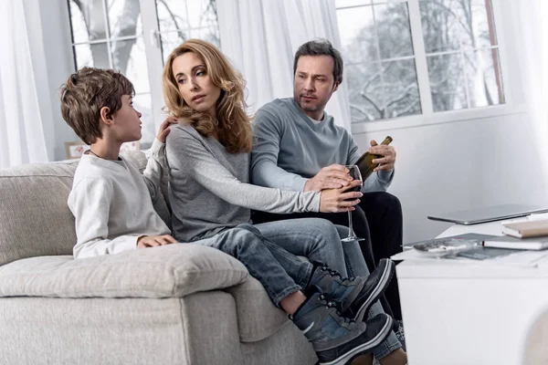 Alcoholic woman looking at her son while sitting with a glass