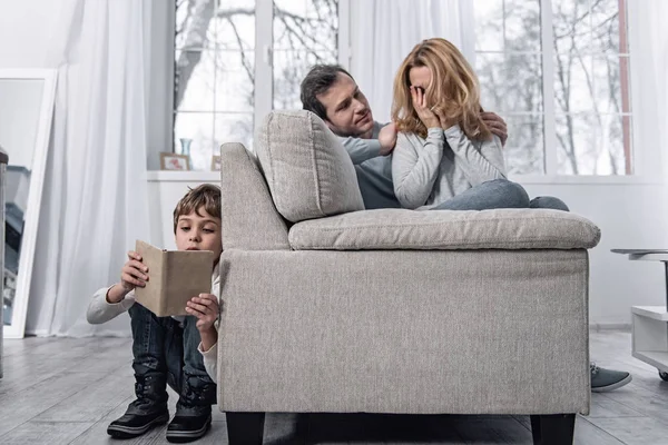 Молода жінка плаче і її син читає книгу за диваном — стокове фото