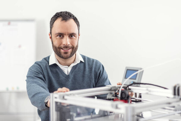 Handsome cheerful man posing near 3D printer
