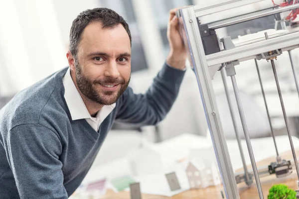 Schöner Mann lehnt sich an 3D-Drucker und lächelt — Stockfoto