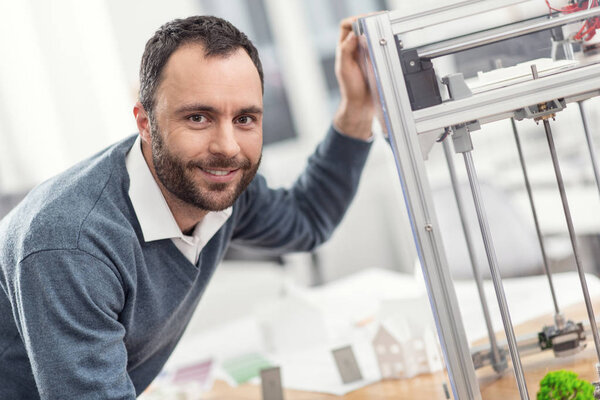 Handsome man leaning on 3D printer and smiling
