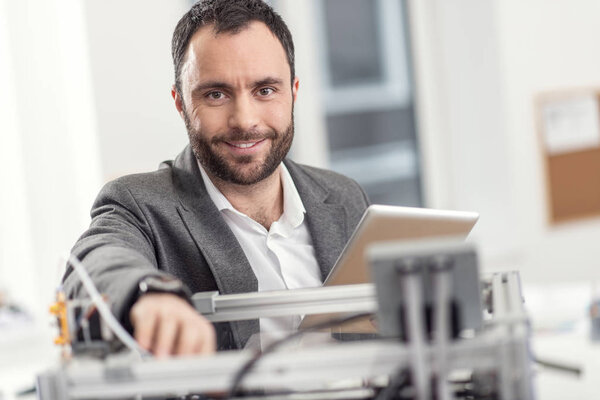 Pleasant man posing while solving problems with 3D printer