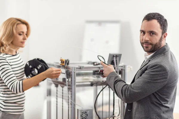 Angenehmer Mann posiert, während er 3D-Drucker für die Arbeit vorbereitet — Stockfoto