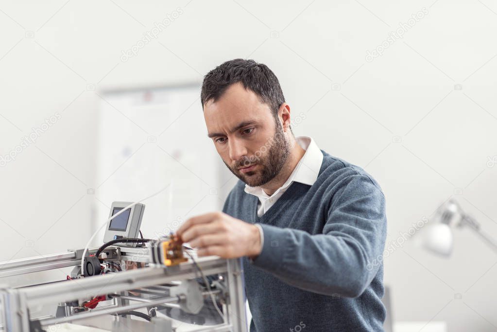 Serious young engineer getting 3D printer ready for work