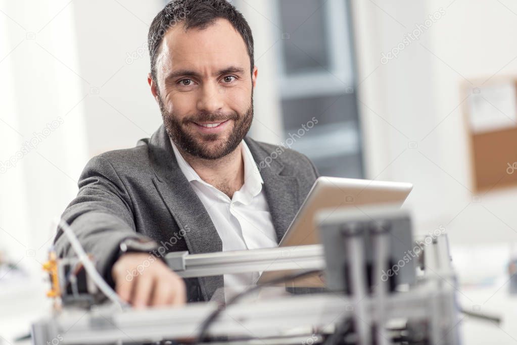 Pleasant man posing while solving problems with 3D printer